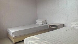 Ein Zimmer mit zwei Betten, einem größeren und einem kleineren, mit weißer Bettwäsche. Zwischen den Betten befindet sich ein Nachttisch mit einer Lampe.