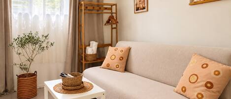 Un salón con sofá, una mesita, una planta y una estantería de madera con adornos.