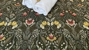 Un lit bien fait, avec une literie à motifs floraux, deux oreillers et un petit bouquet de fleurs et de serviettes.