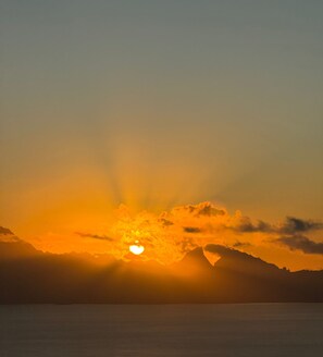 Un coucher de soleil sur une étendue d’eau, avec des montagnes en arrière-plan.