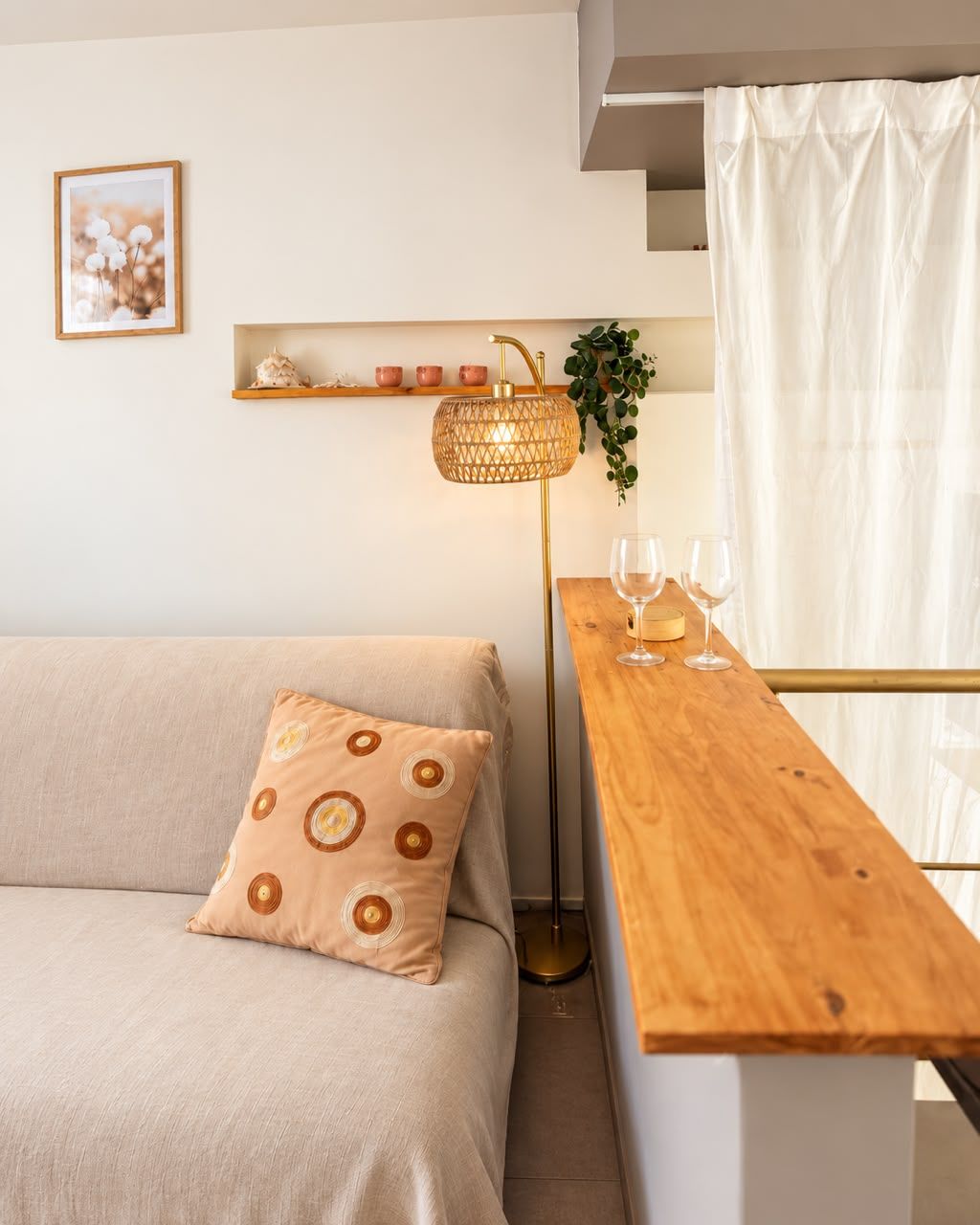 Ein zeitgemäßer Wohnraum mit einer Couch, einem Holztisch mit Gläsern, einer Stehlampe und einem Regal mit Dekoration.