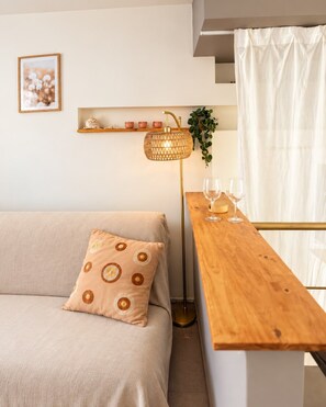 Un espace de vie moderne comprenant un canapé, une table d’appoint en bois avec des verres, une lampe sur pied et une étagère ornée d’objets décoratifs.