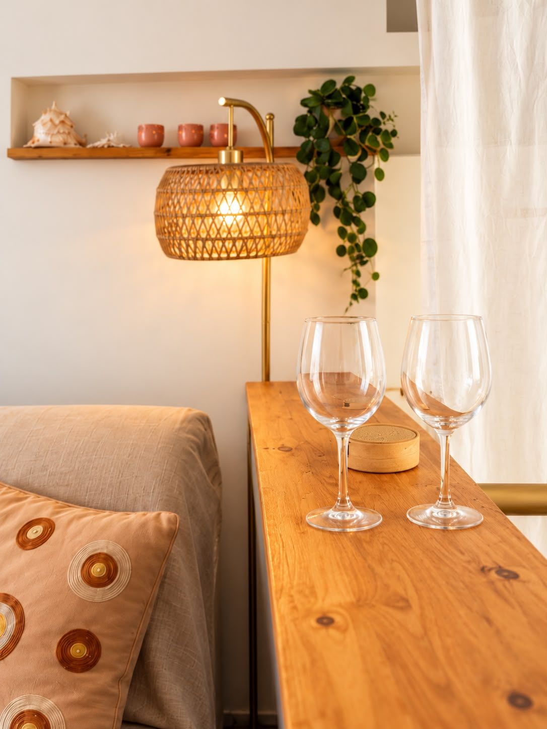 Una stanza ordinata con un letto, un comodino in legno, due bicchieri da vino, una lampada e uno scaffale con oggetti decorativi.