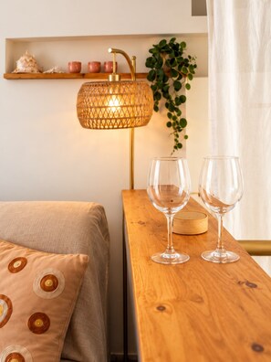 Ein ordentlich eingerichteter Raum mit einem Bett, einem Nachttisch aus Holz, zwei Weingläsern, einer Lampe und einem Regal mit Dekoration.