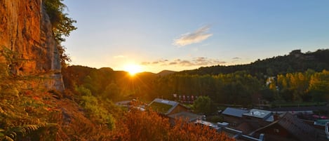 A mountainous landscape with a sunset, buildings with green roofs, and dense forest.
