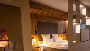 A modern hotel room with a wooden headboard, a bed with white linens, a small round table, and a chair. - Apartment 9 - GUESTHOUSE FELSENLAND (Dahn)