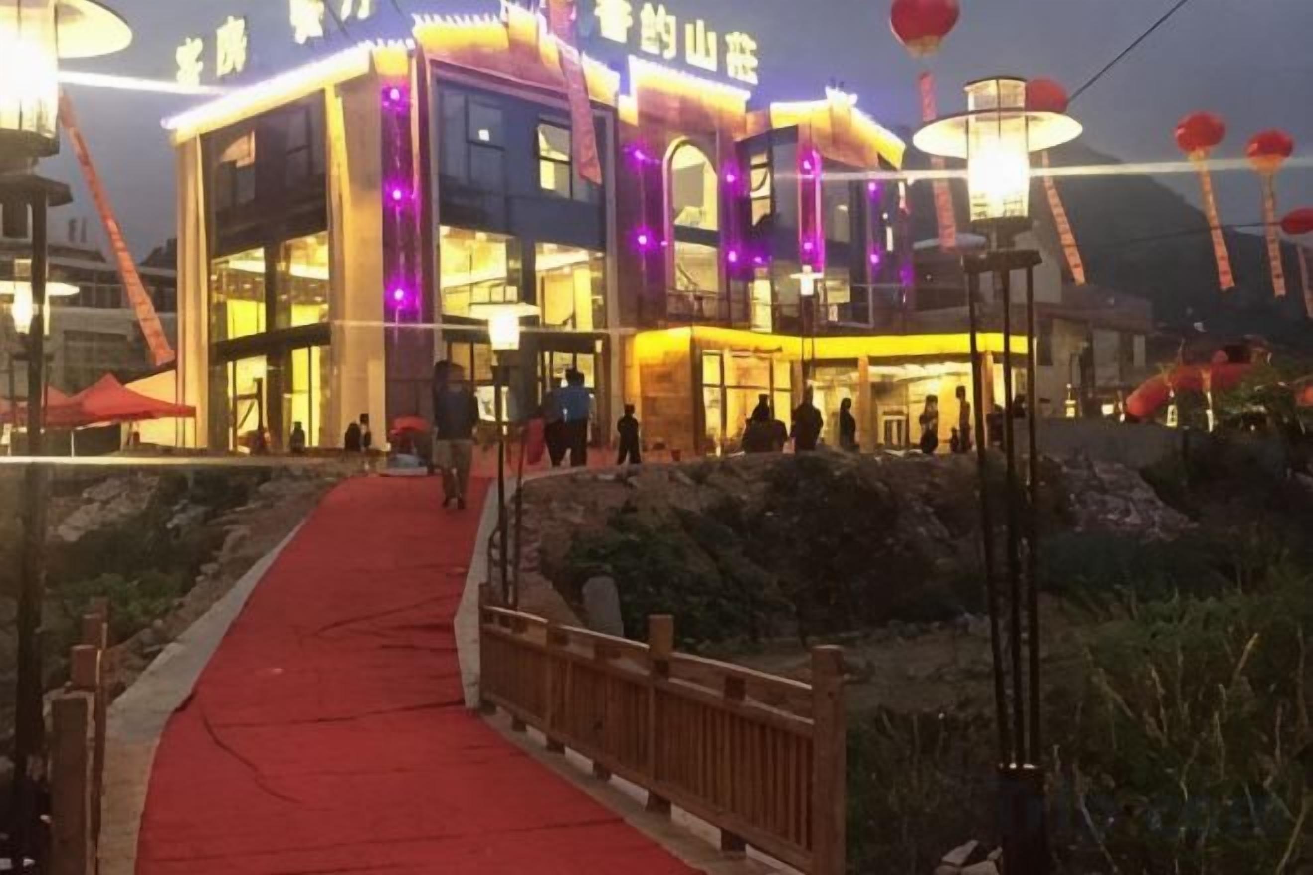 A building with a red carpet pathway leading to the entrance, a wooden fence, and a lamp post.