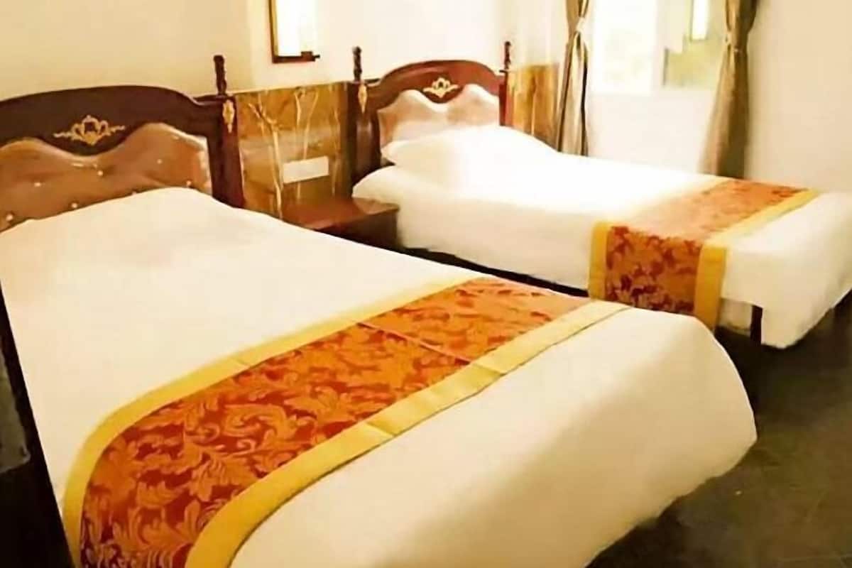 Een hotelkamer met twee enkele bedden, een houten hoofdbord en een raam met gordijnen.
