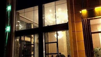 A building facade with large windows, a visible interior with a chandelier, and a door with a person at the entrance.