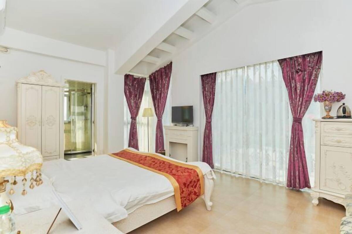 Een slaapkamer met een bed, een televisie, een kledingkast en een groot raam met gordijnen.