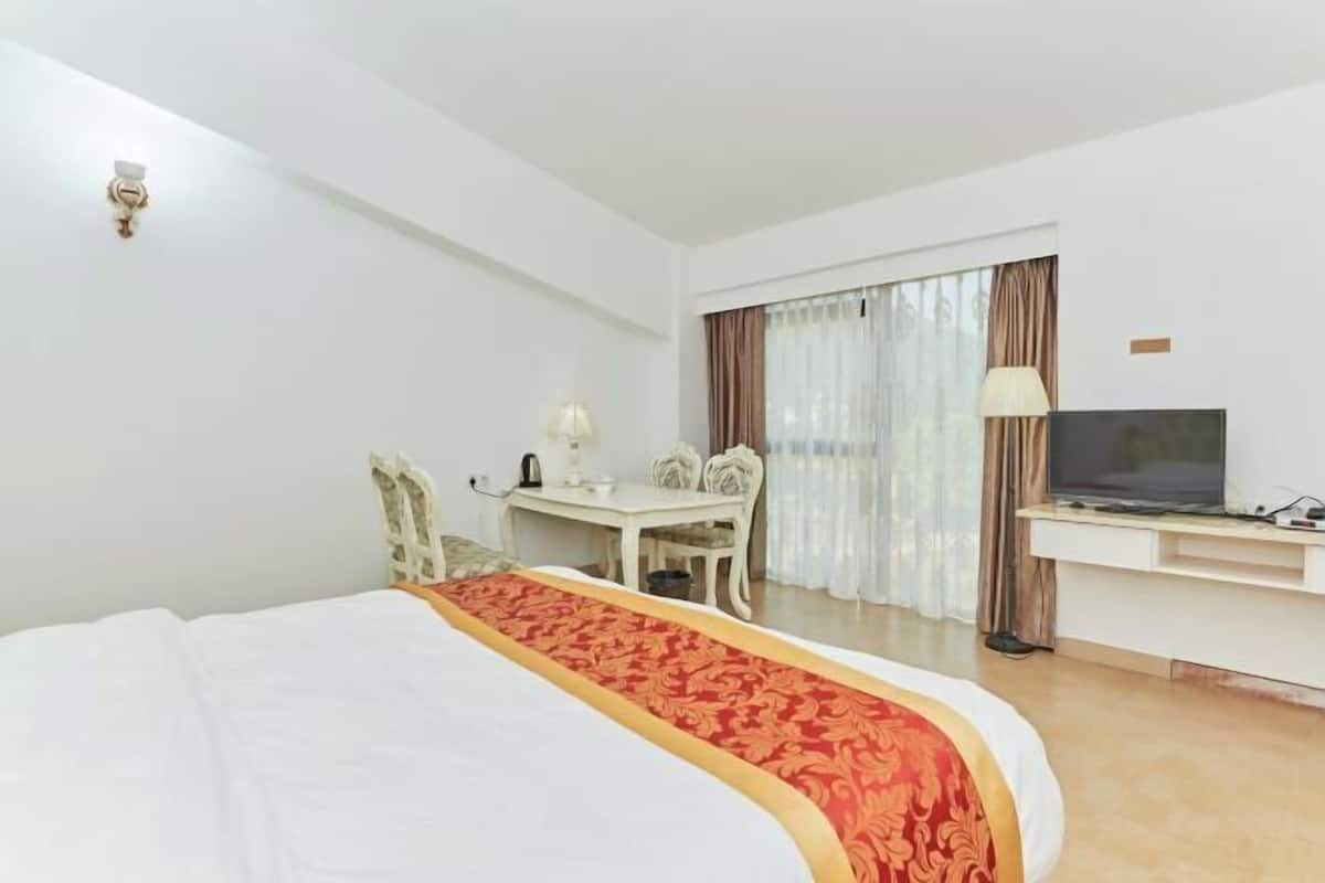 Een hotelkamer met een bed, een bureau, een stoel, een televisie en een raam met gordijnen.
