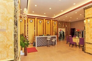 Un vestíbulo de hotel con una recepción, zona de estar y relojes de pared decorativos.