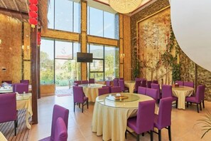 A restaurant with round tables and purple chairs, large windows, and a TV screen. - Xiangyue Villa Hotel (Pinghe)