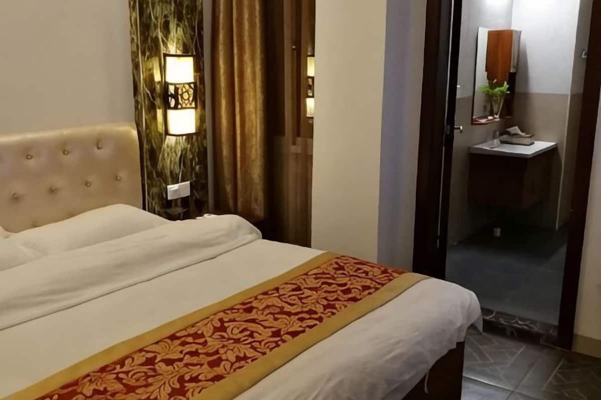 Een hotelkamer met een bed, nachtkastje, lamp, en zichtbare badkamer achter een glazen deur, evenals een spiegel.