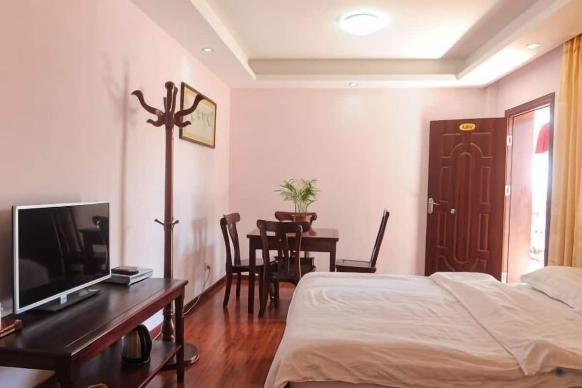 A hotel room with a bed, a desk with a TV, a coat rack, a dining table with chairs, and a door.