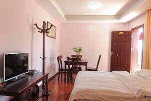 Una habitación de hotel con cama, escritorio con televisor, perchero, mesa de comedor con sillas y una puerta.