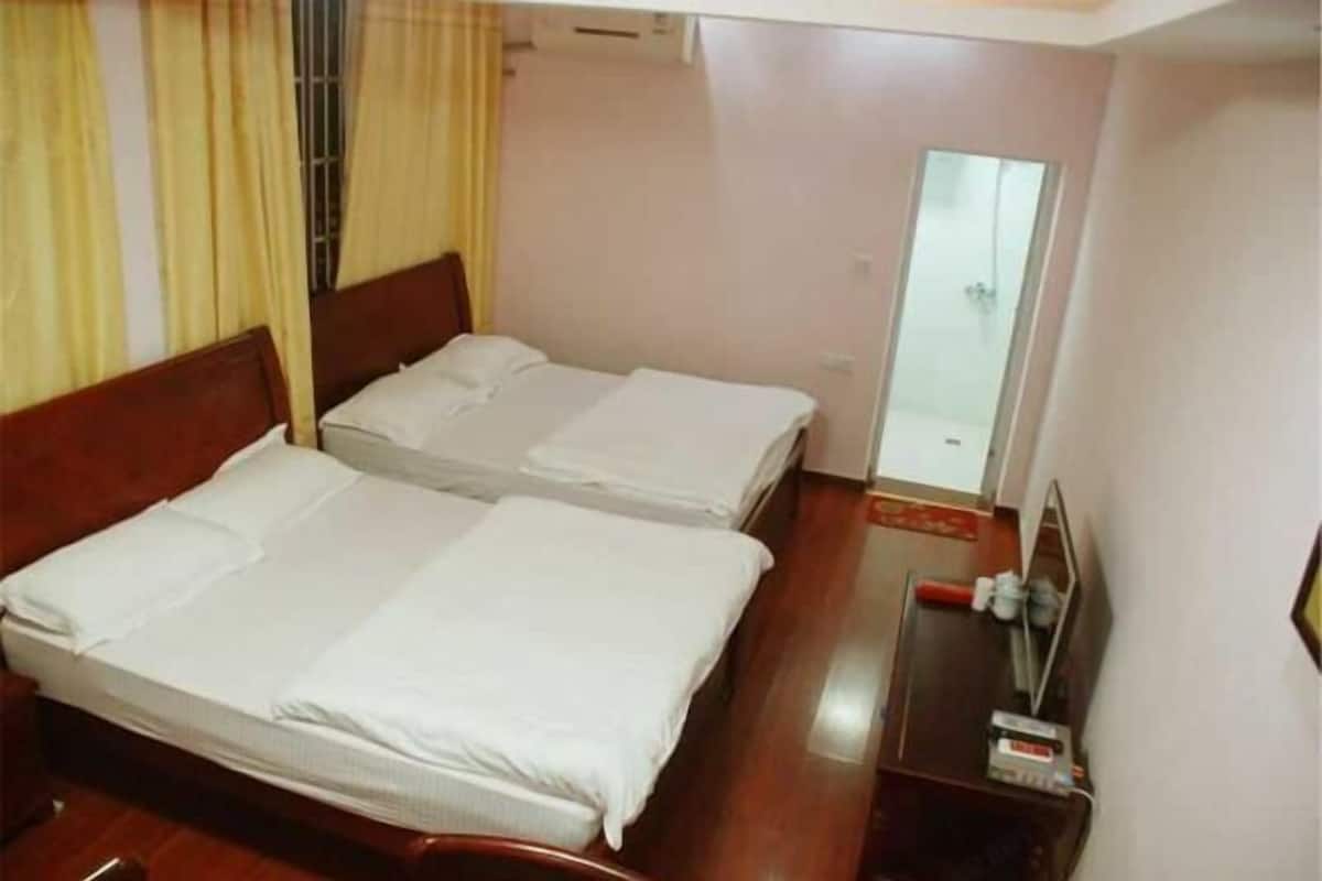A hotel room with two single beds, a wooden headboard, a small table with a mirror, and a window with curtains.