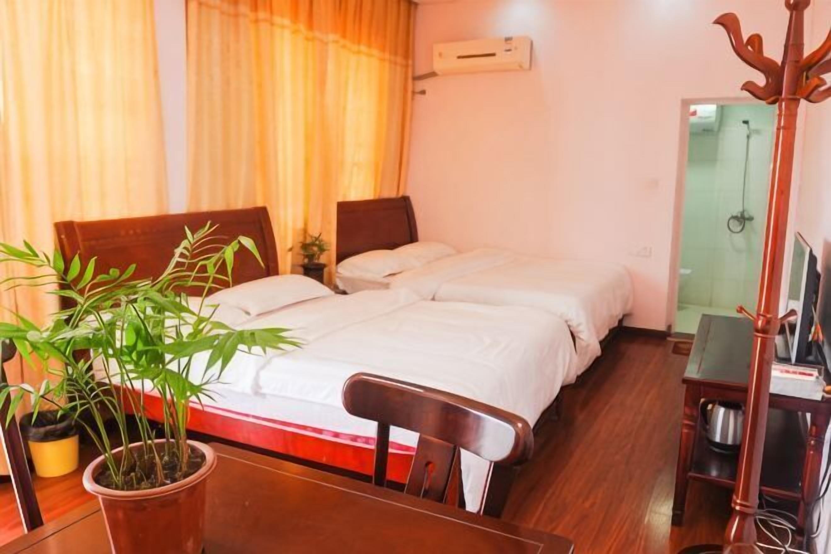 A hotel room with two beds, a wooden table, a potted plant, a chair, a TV, and a shower area.