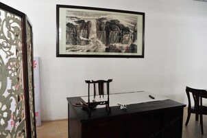 Una habitación con un cuadro enmarcado en la pared, un escritorio con una silla y un separador decorativo.