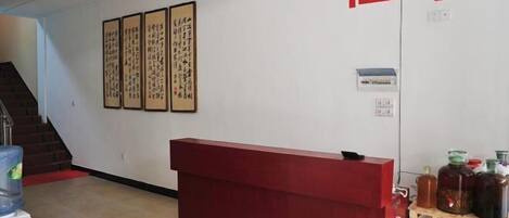 Un área de recepción con un escritorio rojo, una escalera y arte caligráfico en la pared.