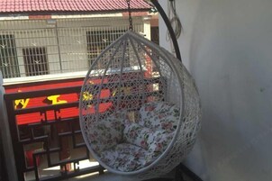 Una silla colgante con un cojín floral, una barandilla roja y amarilla, y una reja metálica al fondo.