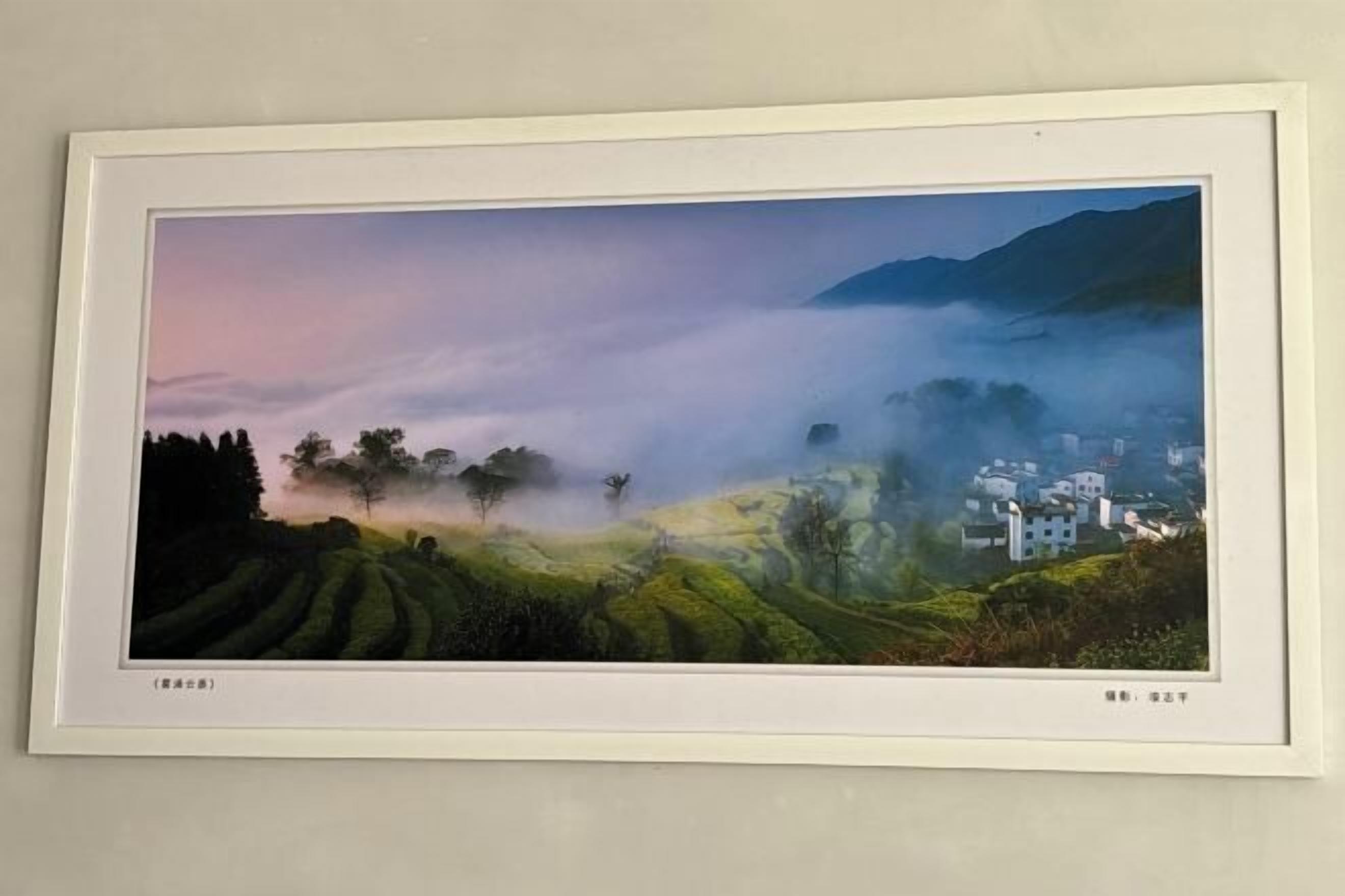 A framed landscape painting of a misty hillside with terraced fields and a village.
