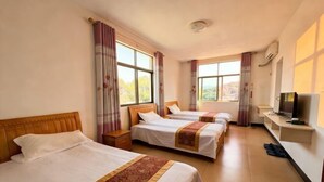 Habitación de hotel con tres camas, televisión y ventana con cortinas.