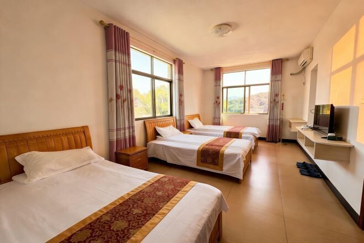 Habitación de hotel con tres camas, televisión y ventana con cortinas.