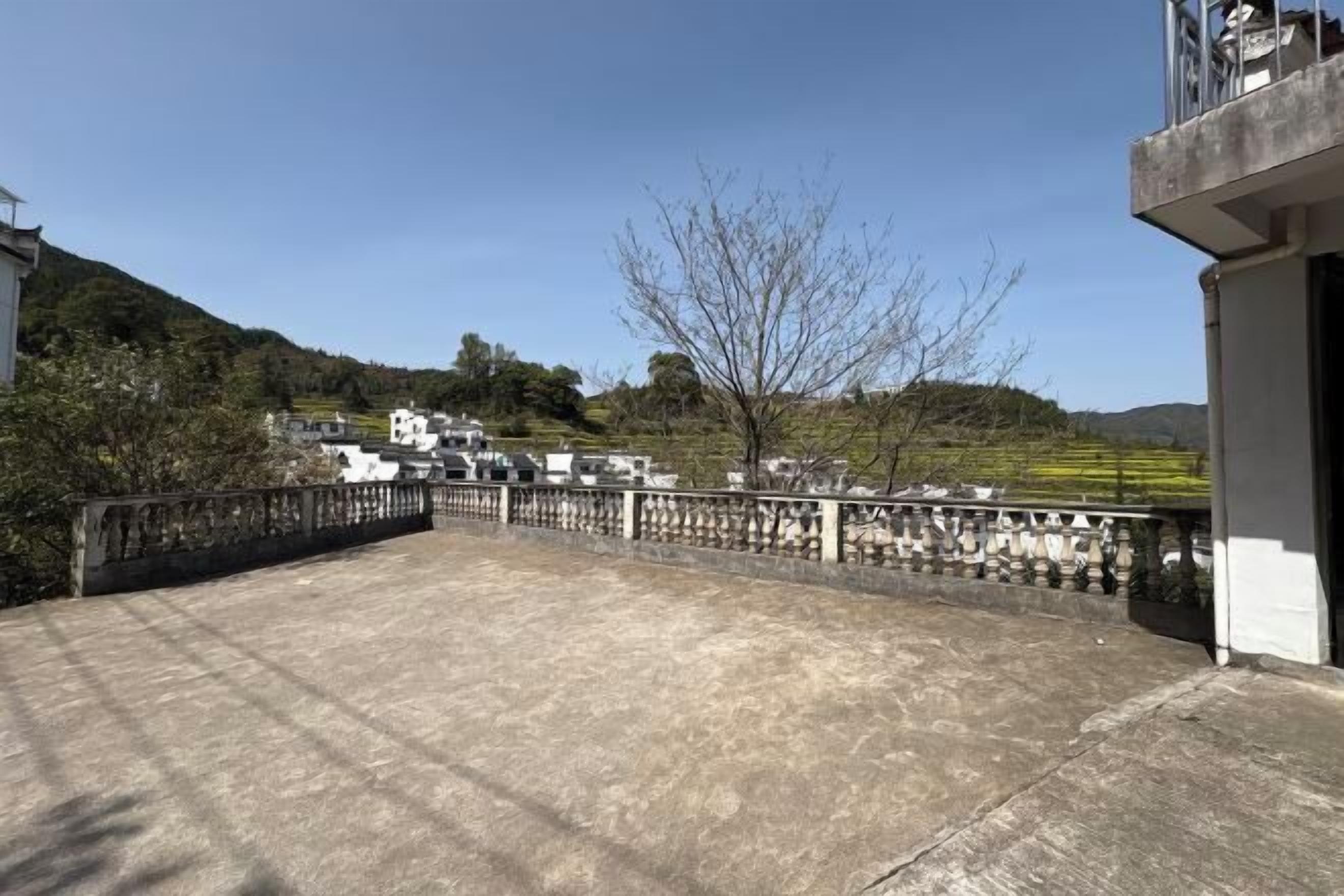 A rooftop terrace with a stone balustrade, a view of a hilly landscape, and buildings in the background.