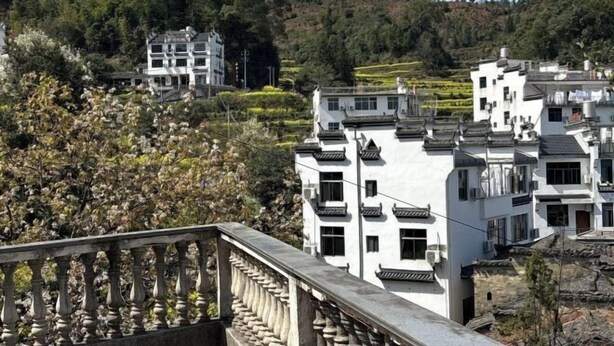 Un edificio tradicional de varios pisos con balcón, rodeado de exuberante vegetación y un paisaje montañoso.