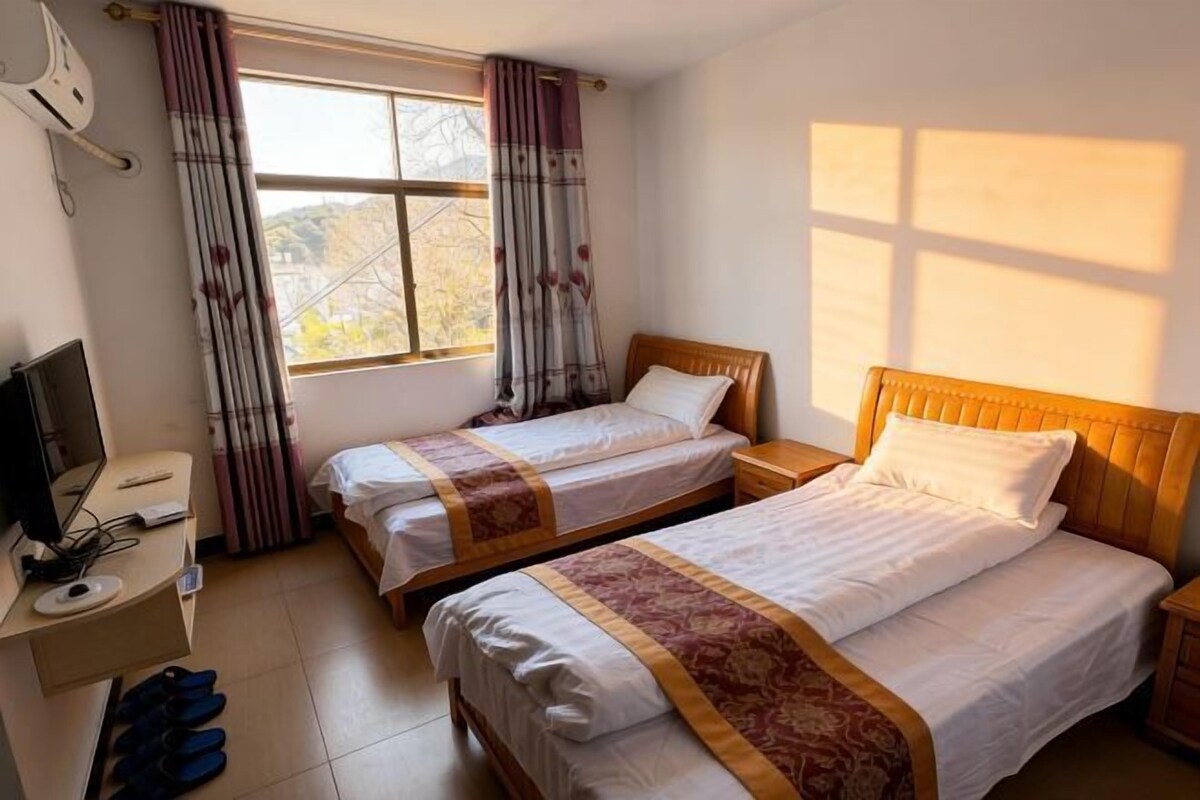 Habitación de hotel con dos camas, un escritorio con computadora, un televisor y una ventana con cortinas.