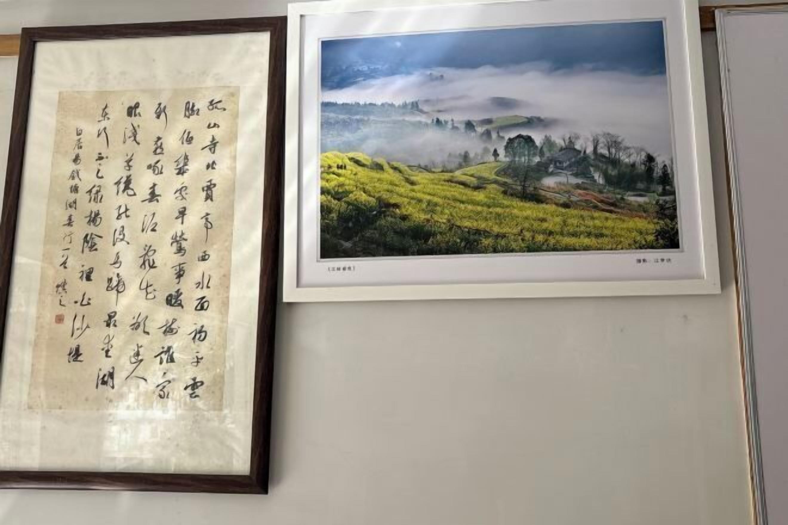 A framed calligraphy piece and a landscape photograph on a wall.