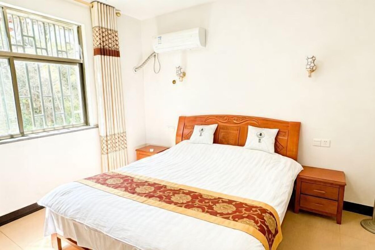 Habitación de hotel con cama, mesita de noche, aire acondicionado de pared y ventana con cortinas.