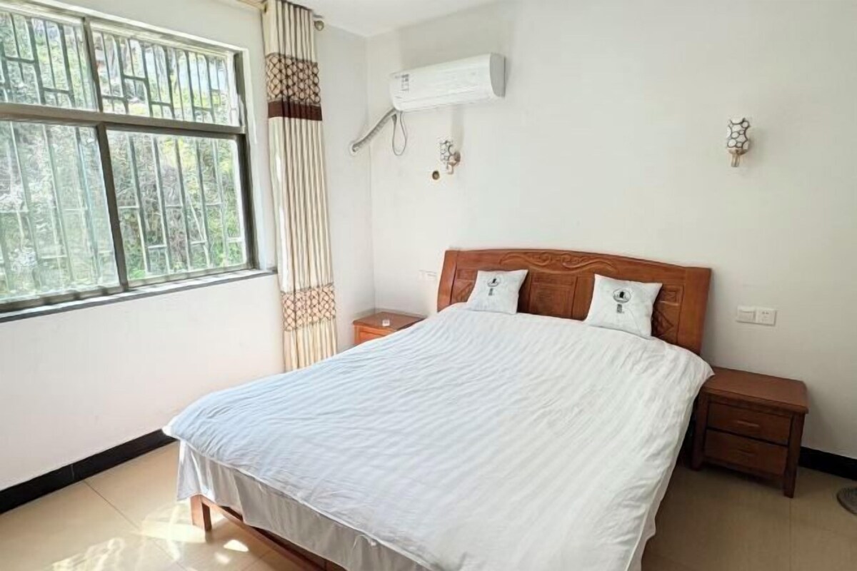 Un dormitorio con una cama, dos mesitas de noche, un equipo de aire acondicionado y una ventana con cortinas.