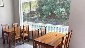 Un área de comedor con una mesa y sillas de madera, un ventanal con vistas a la vegetación y una barandilla de balcón.