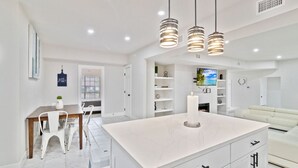 A modern kitchen with a marble island, white cabinetry, and pendant lighting.