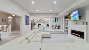 A modern living room with a fireplace, a television, and a kitchen in the background.