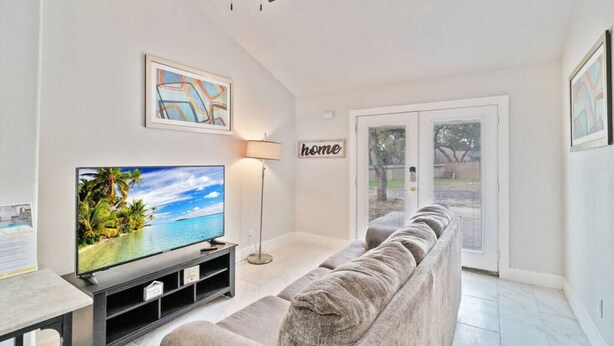 Una sala de estar con televisor de pantalla plana, sofá, lámpara de pie y una puerta con la etiqueta 'home'.