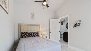 Un dormitorio con cama, ventilador de techo, puerta que da a un baño y un toallero en la pared.