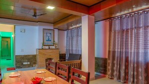 Un comedor con una mesa de madera dispuesta para cuatro, una chimenea y vistas al exterior a través de cortinas estampadas.