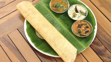 A plate with a rolled food item and three small bowls of sauces on a banana leaf.