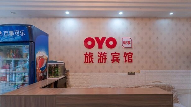 Ein Empfangsbereich mit einem Holztisch, einem Pepsi-Kühlschrank und einer Wand mit OYO-Branding.