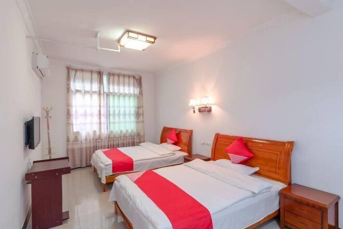 A hotel room with two beds, a desk, a TV, and a window with curtains.