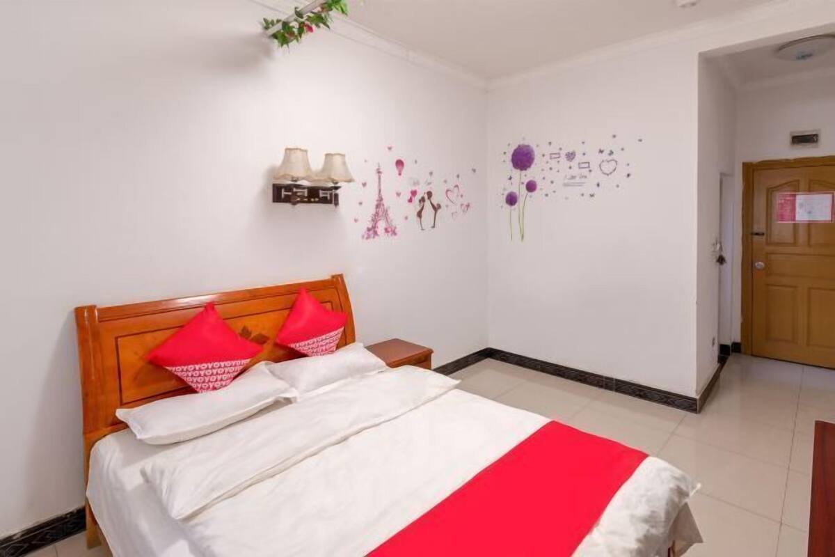 A hotel room with a bed, a nightstand, a wall-mounted lamp, and a door.
