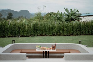 Enjoy a tranquil outdoor dining experience with a bench and table set amidst lush greenery and a distant mountain view.