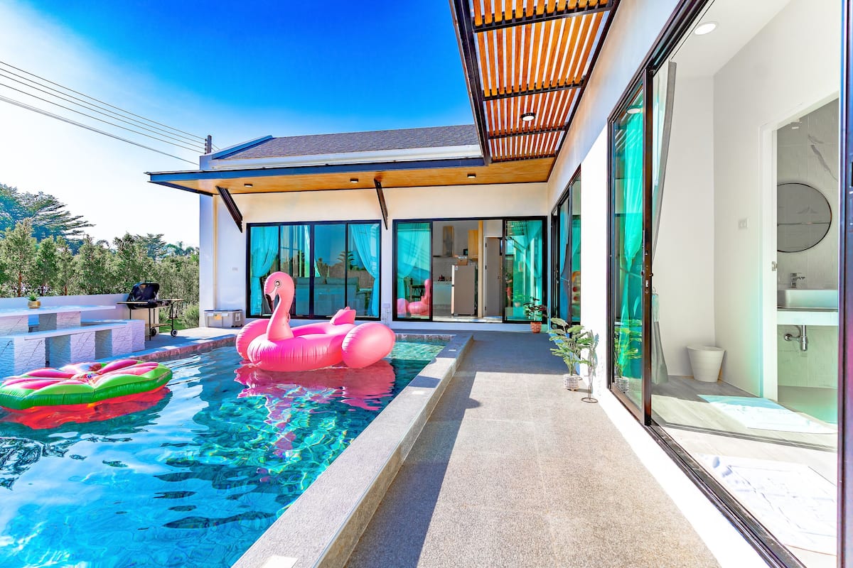 Una casa moderna con piscina, un flotador de flamenco rosa y una pérgola.