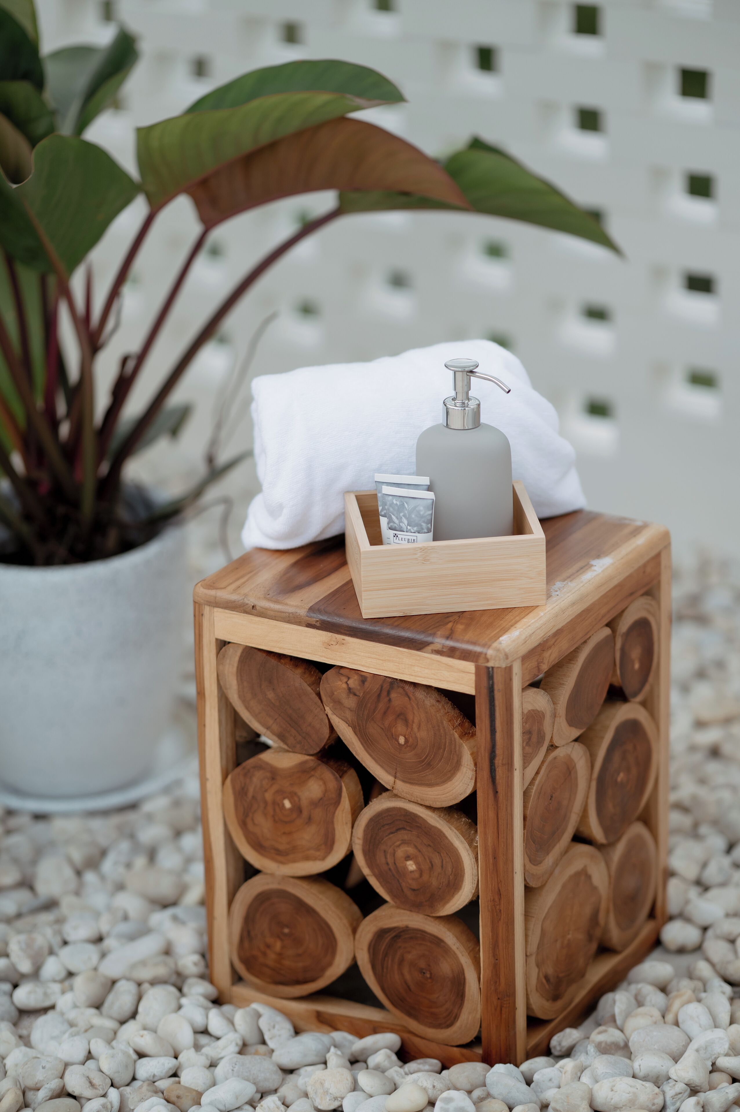 A wooden cube with a bottle and a tissue box on top, surrounded by pebbles and a plant.
