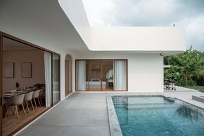 Relax in a spacious living area with a dining set and access to a serene outdoor space featuring a swimming pool.