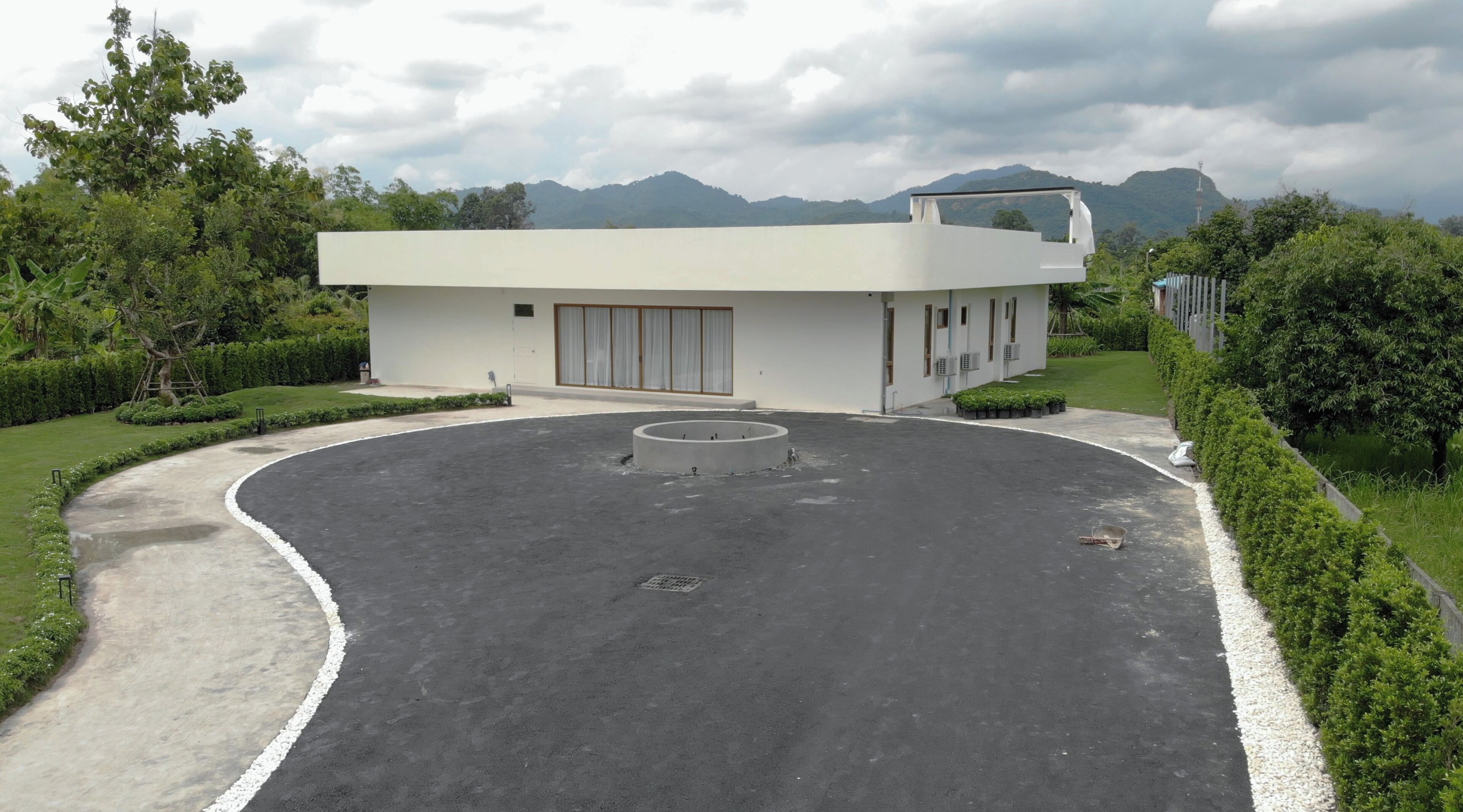 A modern building with a circular driveway, surrounded by well-maintained greenery and a mountainous backdrop.