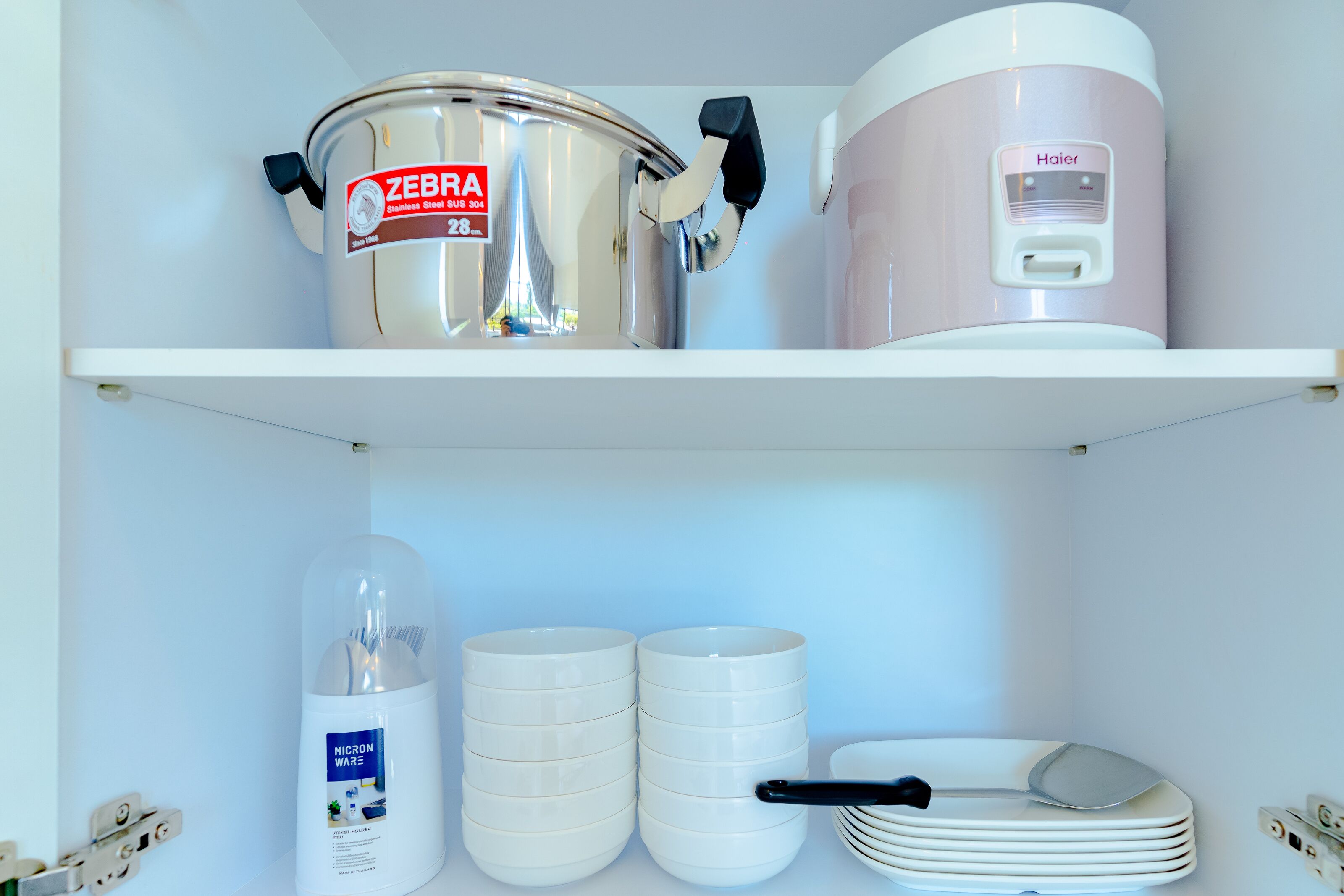 Une étagère de cuisine avec une casserole en acier inoxydable, un cuiseur à riz et une pile d’assiettes.